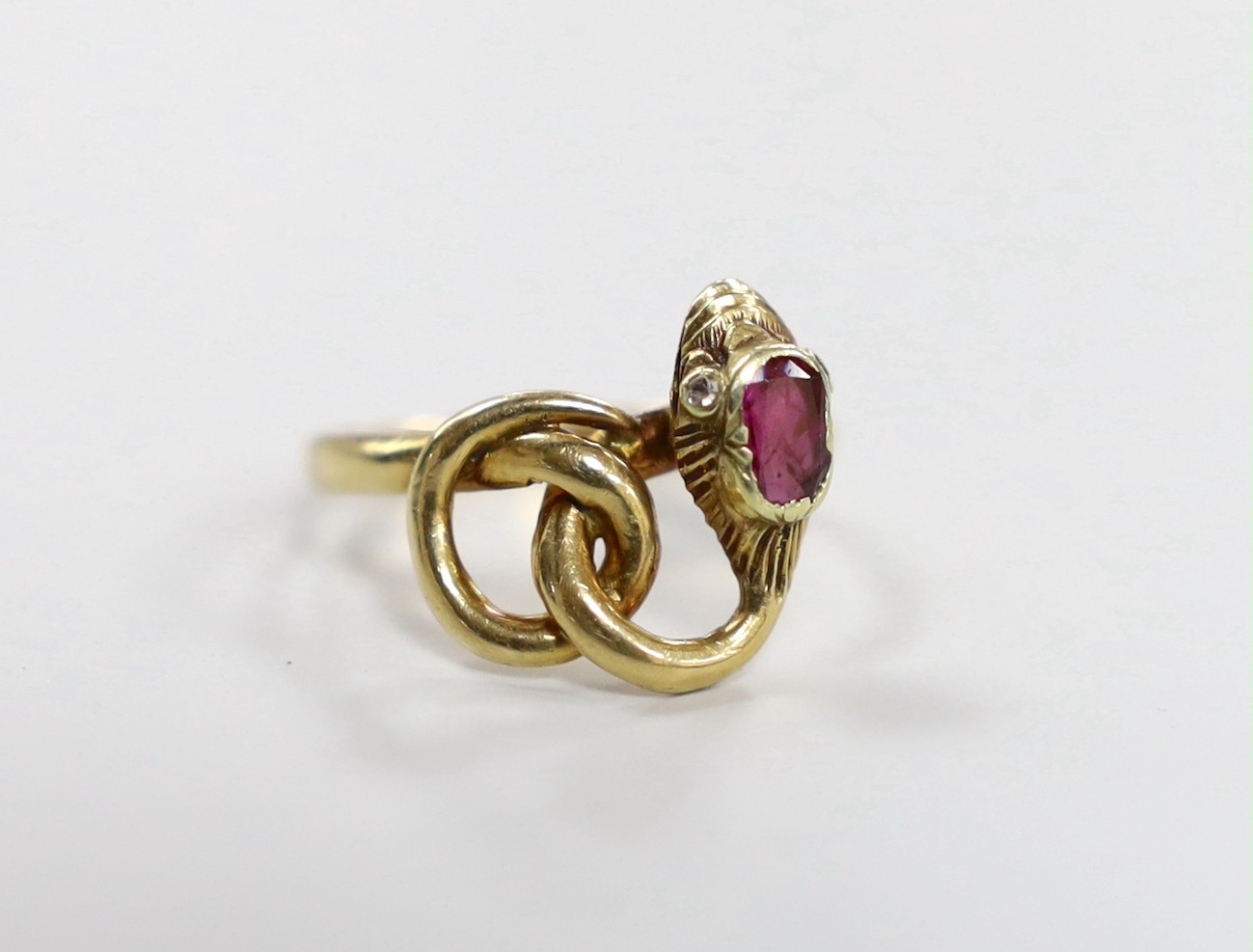 An early 20th century yellow metal and single stone garnet set entwined serpent ring, with diamond chip eyes, size O, gross weight 3.7 grams.